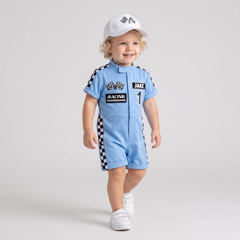 May include: A light blue short-sleeve racing romper with black and white checkered side panels, featuring the text JAKE, RACING, and a checkered flag graphic on the chest. The outfit includes a matching white baseball cap with a checkered flag logo.