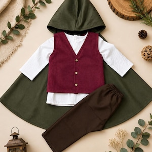 Puede incluir: Un conjunto compuesto por una capa con capucha de color verde oscuro, una camisa blanca de manga larga, un chaleco burdeos con tres botones claros y pantalones de color marr&oacute;n oscuro. Las prendas est&aacute;n dispuestas planas, mostrando el conjunto.