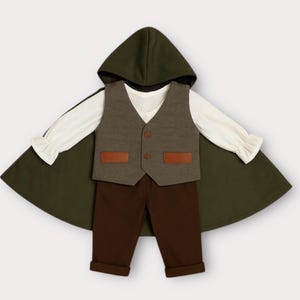 May include: A set consisting of a dark olive green hooded cloak, a cream-colored long-sleeve shirt with ruffled cuffs, a grey vest with two brown rectangular pockets and two buttons, and solid dark brown trousers with cuffed hems.