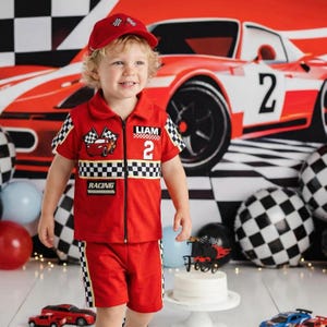 May include: A red short-sleeved collared shirt and matching shorts set featuring a black and white checkered pattern on the sleeves and waist. The shirt includes a zipper, a racing car graphic, the name LIAM, the number 2, and the word RACING.