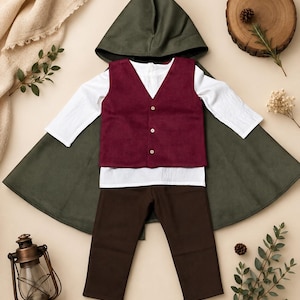 Puede incluir: Un conjunto de disfraz que incluye una capa con capucha de color verde oliva oscuro, una camisa blanca de manga larga, un chaleco burdeos con tres botones claros y pantalones de color marr&oacute;n oscuro. El conjunto se muestra extendido.