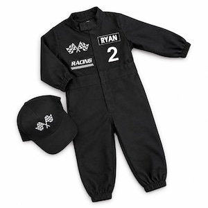 Op de afbeelding: Een zwarte jumpsuit met lange mouwen, elastische boorden en een bijpassende baseballpet. De jumpsuit heeft een witte patch met gekruiste geblokte vlaggen, een RACING-patch, de naam RYAN en het cijfer 2. De pet heeft een geblokt vlag-embleem.