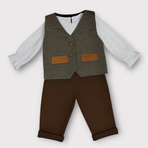 May include: A long-sleeved white shirt with ruffled cuffs layered under a dark olive green vest featuring two brown buttons and two rectangular tan pockets. The outfit includes solid dark brown trousers with cuffed hems at the bottom.