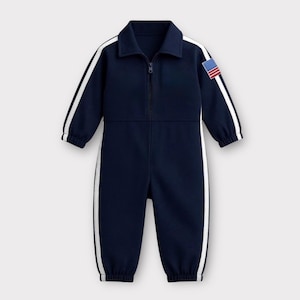 Puede incluir: Mono azul marino con rayas blancas en las mangas y los lados. Cuenta con cuello, cremallera completa y un parche de la bandera estadounidense en la manga superior izquierda. El mono está diseñado para niños.