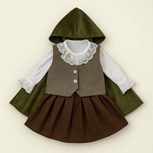 May include: A child's costume set comprising a green hooded cape, a brown waistcoat with two buttons, a white blouse with lace trim, and a brown skirt. The outfit is designed for a child.
