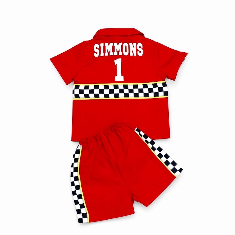 May include: A red short-sleeved collared shirt and matching shorts set. The shirt features the white text SIMMONS above the number 1 and a black and white checkered stripe. The shorts have matching black and white checkered side panels.