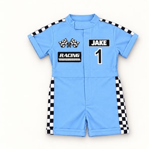 May include: A light blue short-sleeve romper featuring black and white checkered trim along the shoulders and sides. The front displays two crossed checkered flags, the text "RACING", the name "JAKE", and the number "1" in a bold black font.