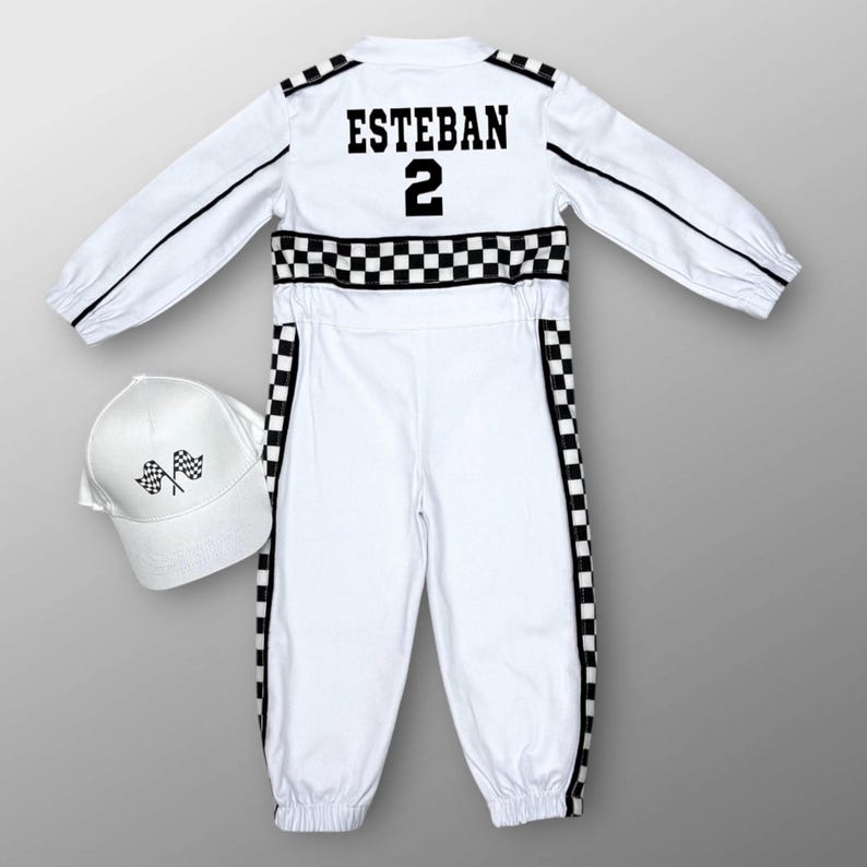 May include: White racing suit with black checkered accents and the name "ESTEBAN" and the number "2" on the back. Includes a matching white baseball cap with checkered flags. The suit has black stripes down the sleeves and legs.