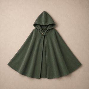 Peut inclure: Une cape à capuche vert forêt présentant une silhouette évasée en forme de A et une fermeture à bouton métallique unique au niveau de l'encolure. Le vêtement est confectionné dans un tissu uni à la texture douce, tombant en une forme large.