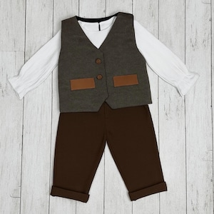 May include: A long-sleeved white shirt with ruffled cuffs paired with a dark gray vest featuring two brown rectangular pockets and two brown buttons. The outfit includes solid dark brown trousers with cuffed hems, creating a complete set.