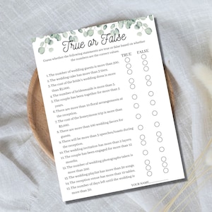Op de afbeelding: Een witte True or False trouwspelkaart met een eucalyptusbladontwerp. De kaart bevat een lijst met uitspraken over de bruiloft, met True en False bellen voor gasten om te beantwoorden. Een leuke activiteit voor een bruidsdouche of huwelijksreceptie.