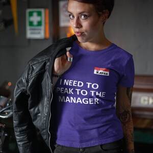 Pu&ograve; includere: Maglietta viola con il testo "I need to speak to the manager" e un cartellino con il nome rosso che dice "Karen".
