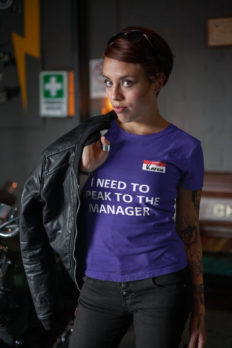 Pu&ograve; includere: Maglietta viola con il testo "I need to speak to the manager" e un cartellino con il nome rosso che dice "Karen".