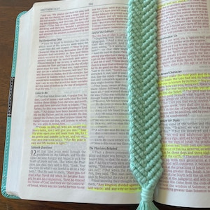 May include: A close-up of a teal blue crochet bookmark with a fringe tassel. The bookmark is placed on an open Bible with the text "Lord of the Sabbath" highlighted.