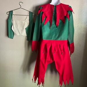 K&ouml;nnte beinhalten: Ein gr&uuml;nes und rotes Elfenkost&uuml;m, bestehend aus einem lang&auml;rmeligen Hemd, einer Hose und einer Weste. Das Hemd hat einen roten Kragen und Manschetten mit goldenen Gl&ouml;ckchen. Die Hose ist rot mit gezackten Kanten und Gl&ouml;ckchen. Die Weste ist gr&uuml;n mit cremefarbenem Futter.