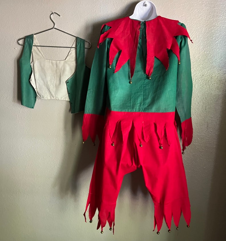 K&ouml;nnte beinhalten: Ein gr&uuml;nes und rotes Elfenkost&uuml;m, bestehend aus einem lang&auml;rmeligen Hemd, einer Hose und einer Weste. Das Hemd hat einen roten Kragen und Manschetten mit goldenen Gl&ouml;ckchen. Die Hose ist rot mit gezackten Kanten und Gl&ouml;ckchen. Die Weste ist gr&uuml;n mit cremefarbenem Futter.