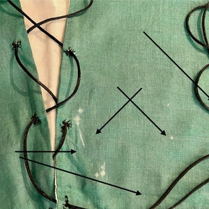 K&ouml;nnte beinhalten: Nahaufnahme eines t&uuml;rkisfarbenen Stoffes mit schwarzer Kordelschn&uuml;rung. Der Stoff hat eine einfarbige t&uuml;rkisfarbene Farbe mit sichtbarer Textur. Die schwarze Kordel ist durch &Ouml;sen an den R&auml;ndern gef&auml;delt und erzeugt ein dekoratives Muster. Der Hintergrund ist ein wei&szlig;er Stoff.