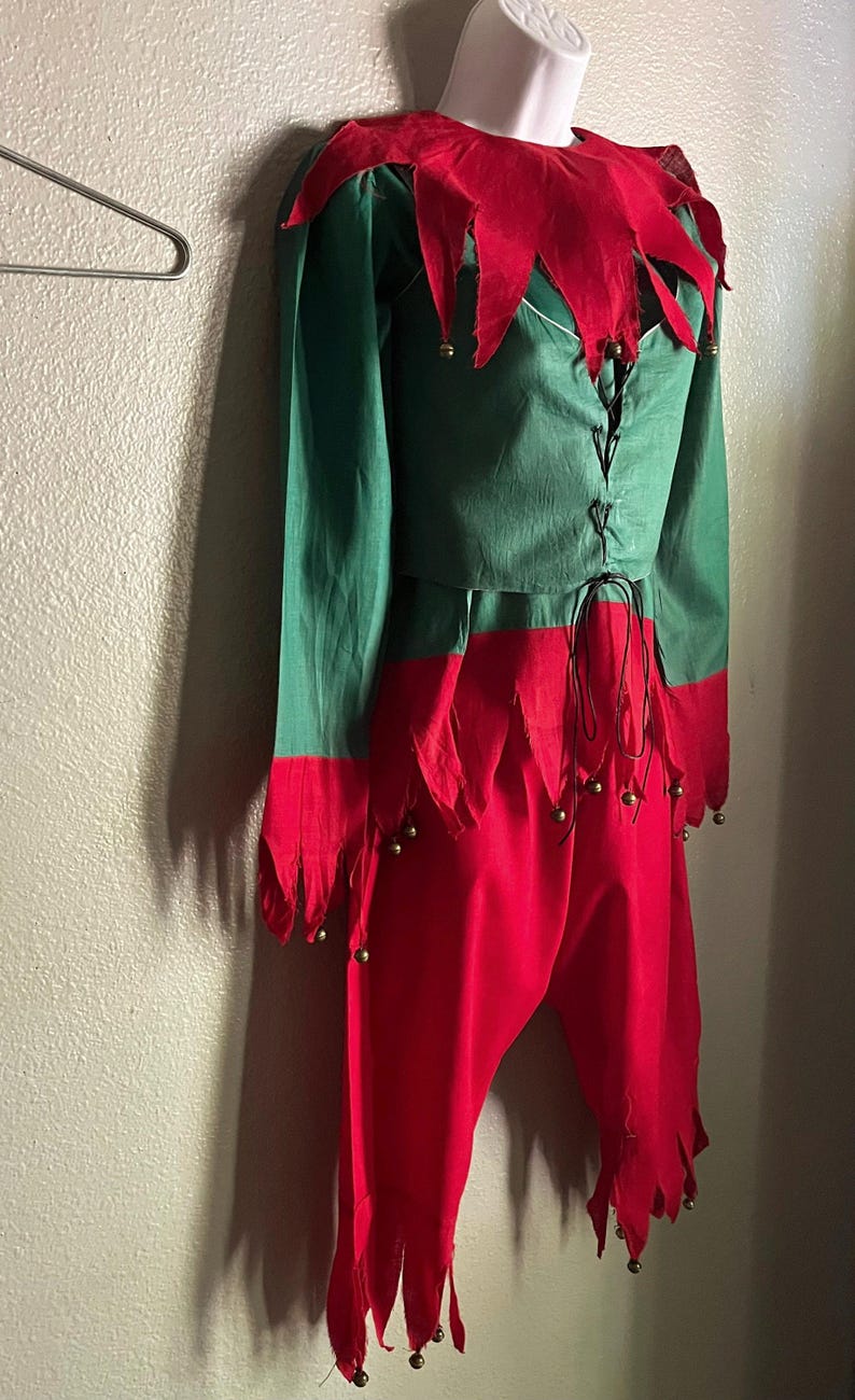 May include: A green and red jester costume with a red collar and bell accents. The costume has a green long-sleeved shirt and red pants with a jagged hem.