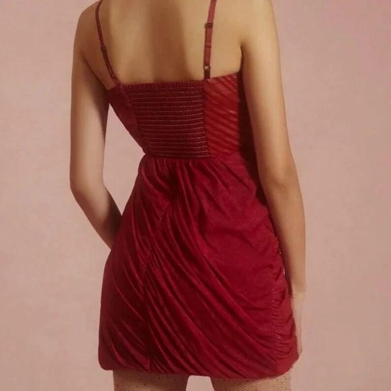 K&ouml;nnte beinhalten: Ein rotes Minikleid mit Spaghettitr&auml;gern und einem gerafften Rock. Das Oberteil hat ein strukturiertes, horizontal gestreiftes Muster. Das Kleid ist aus einem weichen, flie&szlig;enden Stoff gefertigt. Die Tr&auml;ger sind verstellbar.