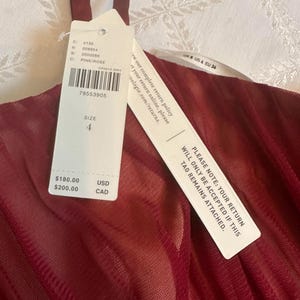 K&ouml;nnte beinhalten: Ein bordeauxfarbenes Kleid mit einem transparenten Overlay und einem angebrachten Etikett. Das Etikett gibt die Kleidergr&ouml;&szlig;e 4 an und enth&auml;lt den Text "PLEASE NOTE: YOUR RETURN WILL ONLY BE ACCEPTED IF THIS TAG REMAINS ATTACHED."