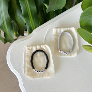 May include: Two bracelets with the letters "I Love PB" spelled out in white beads on black and grey beaded bracelets. The bracelets are in small white drawstring bags.