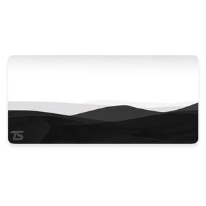 Puede incluir: Alfombrilla de escritorio rectangular con un diseño de paisaje minimalista. El diseño muestra colinas en capas en tonos grises y negros sobre un fondo blanco. La esquina inferior izquierda tiene un logotipo "TS" estilizado.