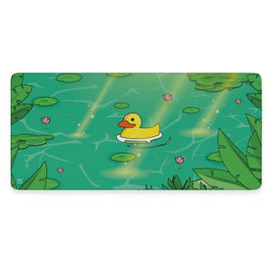 Puede incluir: Un pato de goma de dibujos animados verde y amarillo flota en un estanque con nenúfares y plantas verdes. El estanque está rodeado de follaje verde y el agua es de color verde azulado claro.