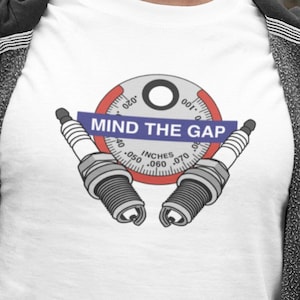 May include: White t-shirt with a graphic of a spark plug gapping tool and the text "MIND THE GAP".
