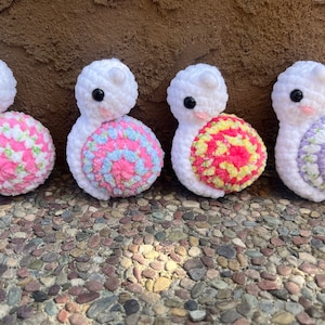 May include: Four crocheted snail plushies with white bodies and colorful shells. The shells are pink and white, blue and pink, pink and yellow, and purple and white.