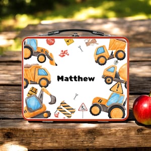 May include: A personalized lunchbox with a construction theme. The lunchbox features illustrations of orange construction vehicles, traffic cones, and road signs. The name "Matthew" is printed in black letters on the front.