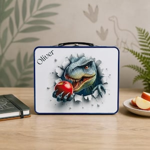 Può includere: Un portapranzo rettangolare in metallo con sfondo bianco e bordo blu scuro. La parte anteriore presenta la grafica di un dinosauro blu e verde che rompe la superficie, tenendo in mano una mela rossa. Il nome Oliver è stampato in testo nero.