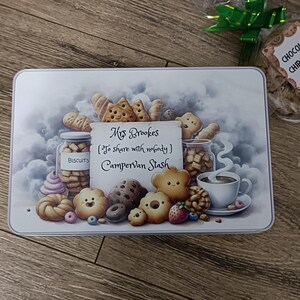 May include: A rectangular tin with a watercolor illustration of various biscuits, cookies, and a cup of coffee. The tin reads "Mrs Brookes (To share with nobody) Campervan Stash". A separate bag contains a chocolate chip cookie.