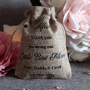 May include: A small hessian bag with a drawstring closure. The bag is decorated with black text that reads "Alfie Thank You for being our Little Best Man Love Daddy & Carol 3rd May 2015".