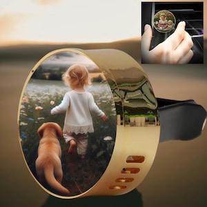 May include: Gold-coloured car air vent clip featuring a circular image of a child and a dog in a field. The clip has a black attachment and a decorative design.