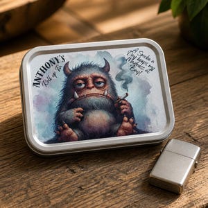 Op de afbeelding: Een rechthoekig metalen blik met een afbeelding van een harig, gehoornd monster dat een rokende sigaret vasthoudt. De tekst luidt "ANTHONY'S Roll up Tin" en "A Smoke a Day keeps my Madness at Bay!". Een zilveren metalen aansteker ligt naast het blik.