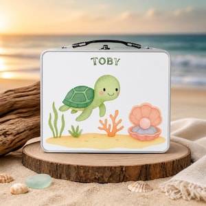 May include: A rectangular metal lunch box with a white background featuring a watercolour illustration of a green sea turtle, orange coral, and a pink seashell with a pearl. The name TOBY is printed in green letters at the top centre.