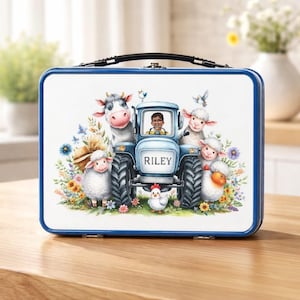 Pode incluir: Uma lancheira azul e branca com uma cena de fazenda extravagante. Um trator azul claro com o nome "RILEY" é cercado por ovelhas de desenho animado, uma vaca e uma galinha. A lancheira tem uma alça preta e uma borda azul.