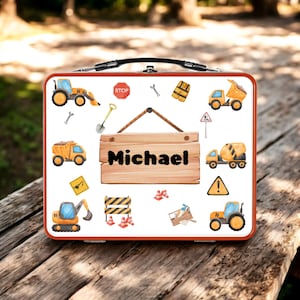 May include: A red and white lunchbox featuring construction vehicles and tools. The lunchbox has a black handle and a wooden sign with the name "Michael" on it. Construction vehicles include a dump truck, excavator, and cement mixer.