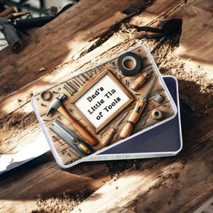 May include: A rectangular tin with a wooden design, filled with miniature tools. The tin features a framed sign that reads "Dad's Little Tin of Tools." Tools include a hammer, screwdrivers, tape, and a ruler. The tin is set on a wooden surface.