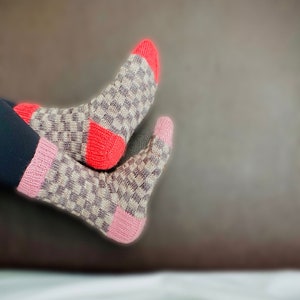 May include: A pair of knitted socks with a checkered pattern in shades of gray, pink, and red.