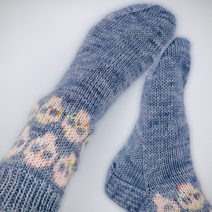 Puede incluir: Un par de calcetines azules de punto con un patrón floral blanco y rosa. Los calcetines están hechos de un material suave y cómodo y son perfectos para mantener los pies calientes en invierno.