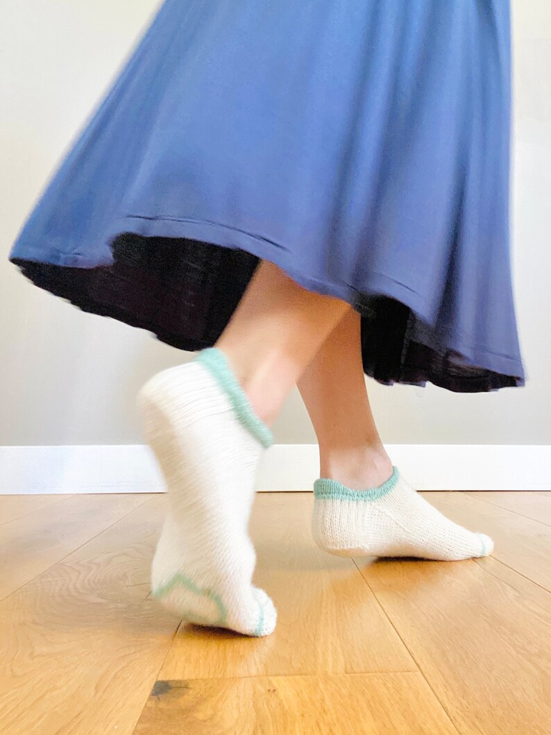 May include: A pair of white ankle socks with a light blue trim. The socks are worn by a person wearing a blue skirt.