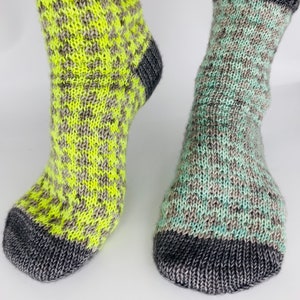 Puede incluir: Dos pares de calcetines de punto con un patrón a cuadros. Un par es gris y verde, el otro es gris y amarillo.