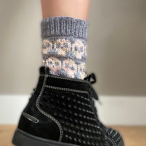 May include: A pair of grey and pink patterned socks with a floral design. The socks are worn with black high-top sneakers with black studs.
