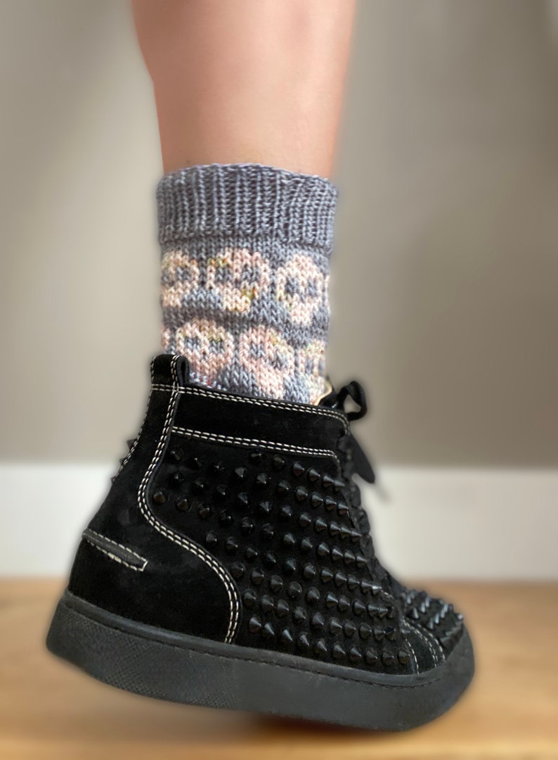 May include: A pair of grey and pink patterned socks with a floral design. The socks are worn with black high-top sneakers with black studs.