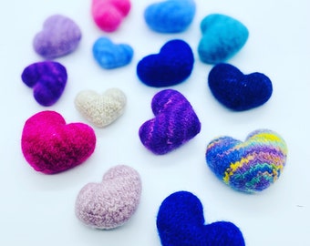 May include: A collection of felt hearts in various colors, including pink, purple, blue, and white. The hearts are arranged in a semi-circle on a white background.