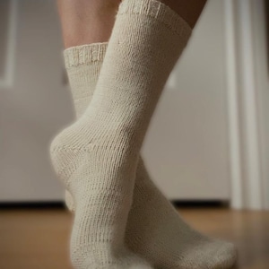 May include: Cream-colored, knitted socks. The socks are knee-high with a ribbed cuff and a textured knit pattern. The socks are made of a soft, warm material, perfect for cold weather.