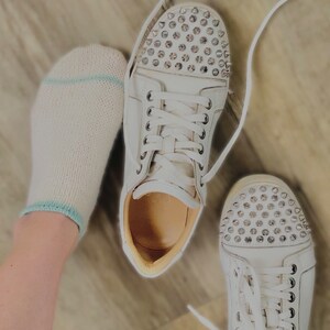 May include: A pair of white sneakers with silver studs on the toe. The sneakers have white laces and are worn with white socks.