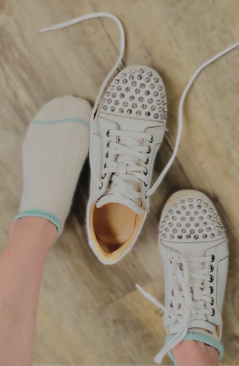 May include: A pair of white sneakers with silver studs on the toe. The sneakers have white laces and are worn with white socks.