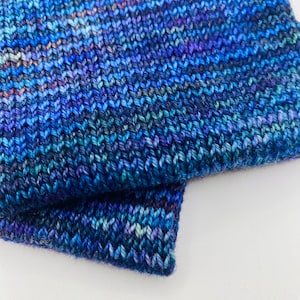 May include: Close-up of a blue knitted fabric with a variegated yarn. The fabric is folded over itself, showing the texture of the knit.
